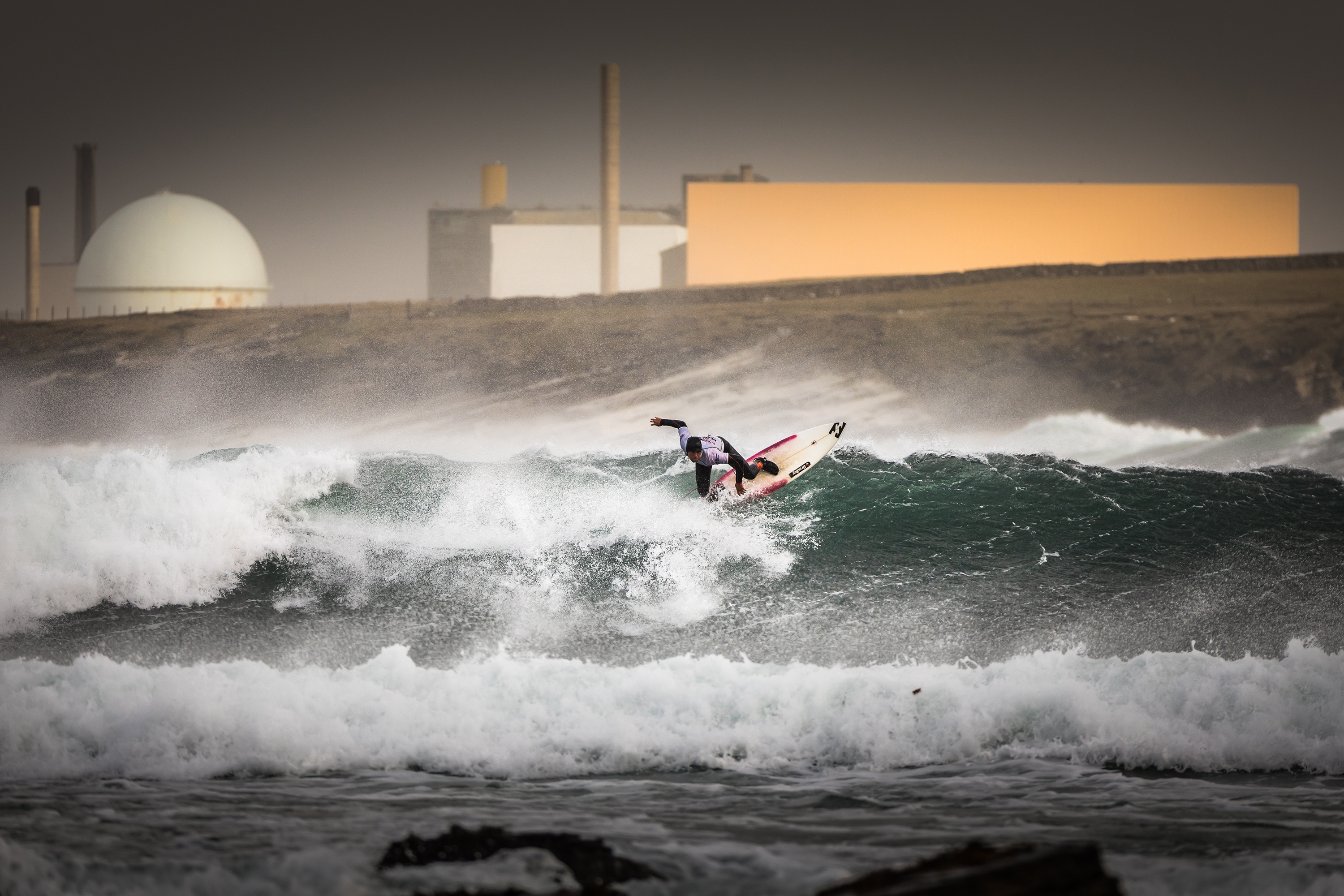 Surfer in big waves with Dounreay in the background